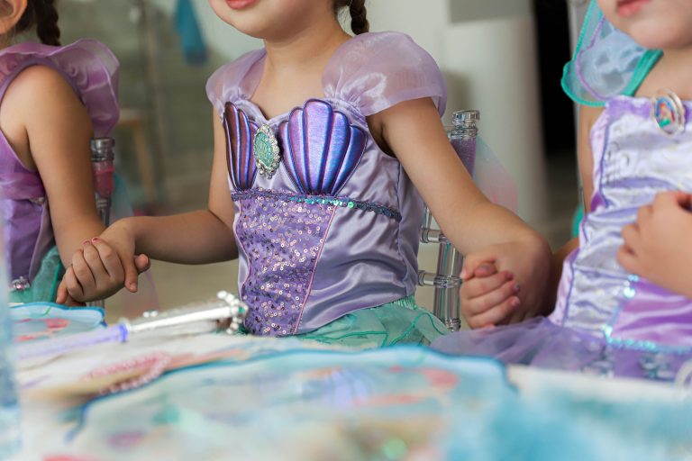 Close-up of three children holding hands at a party, dressed in shimmering mermaid costumes, focusing on their intertwined fingers.